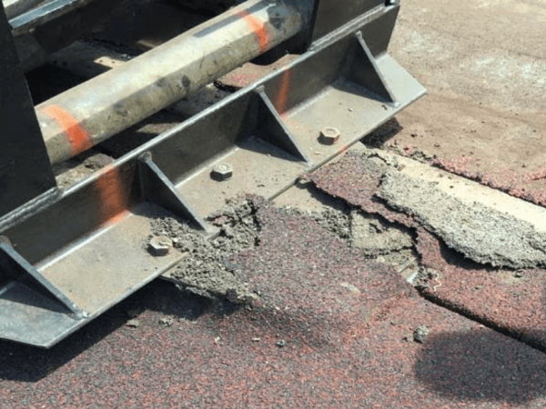 A machine is working on a road with a broken asphalt.