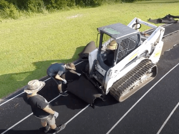 Two men are working on a track with a skid steer.