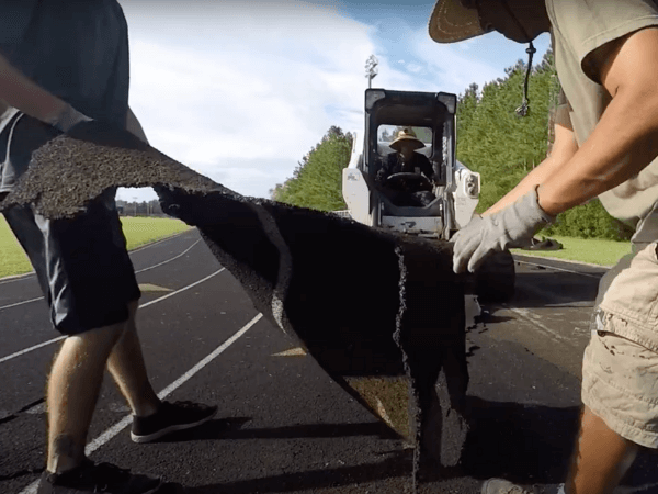 Two men are working on a large piece of asphalt.
