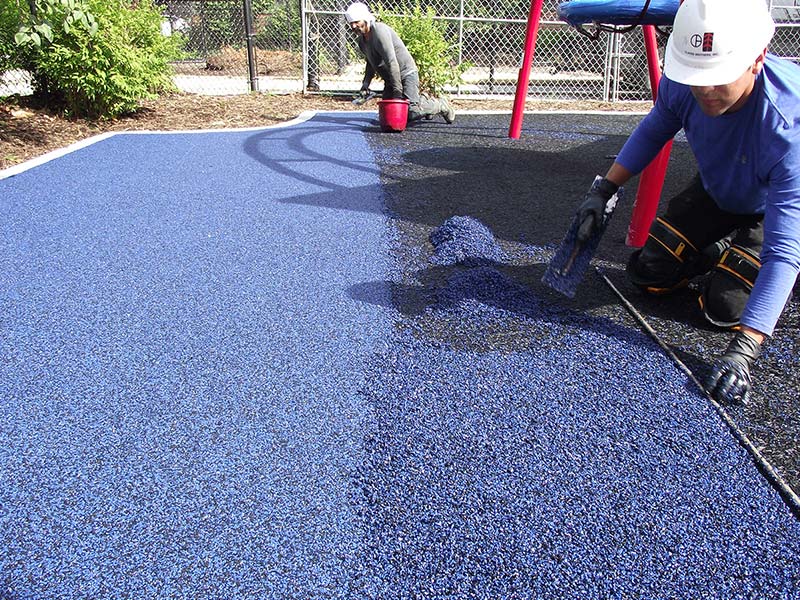A man is working on a playground with blue rubber.